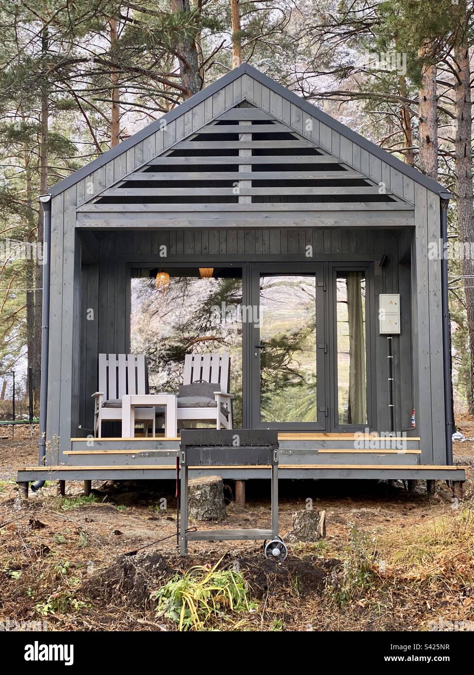 Ein Ferienhaus im Stil eines Bauernhauses mit Glastüren und einer Veranda mit Stühlen im Wald. Stockfoto