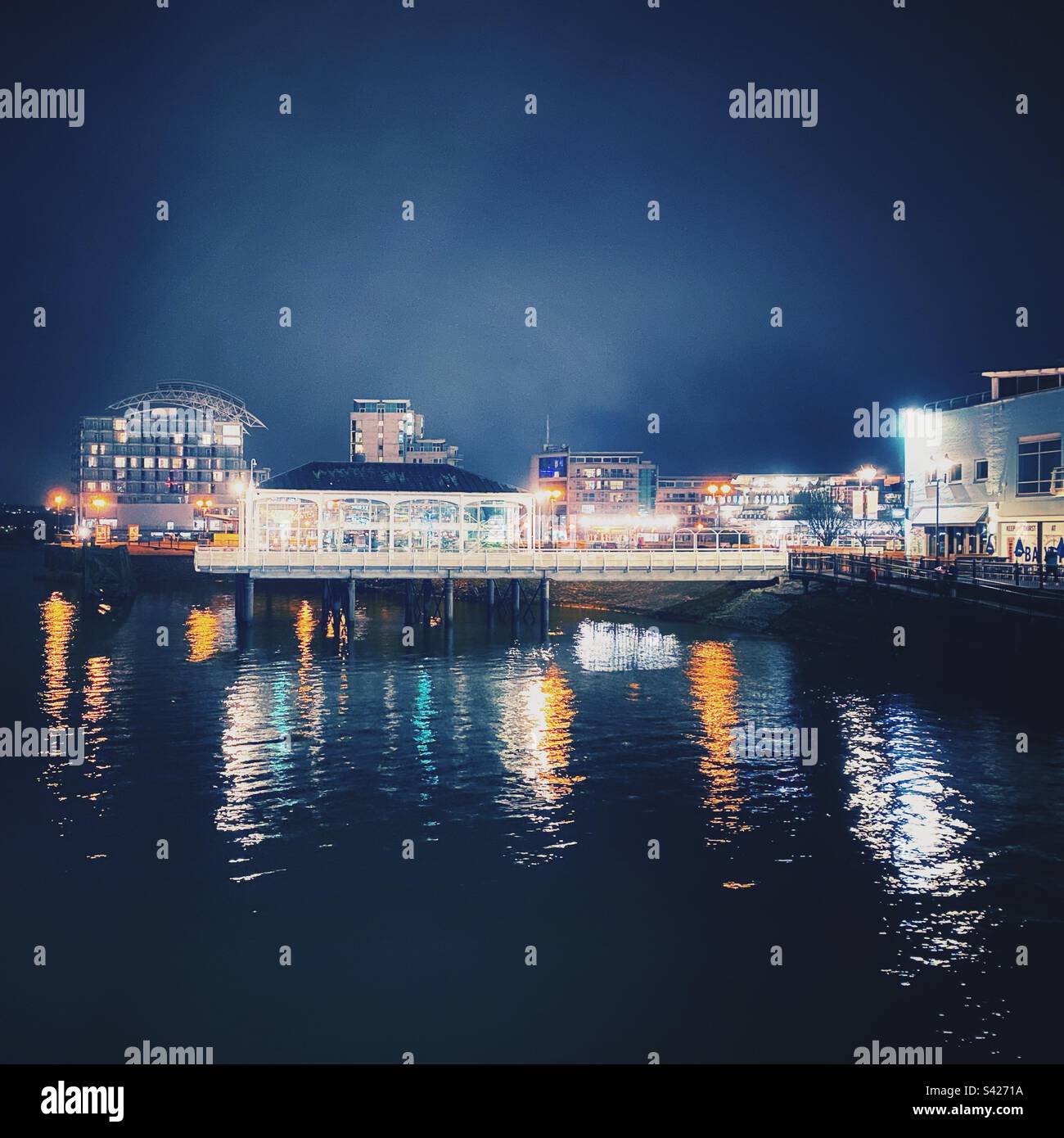 Ein Foto des Restaurantgeschäfts in Mermaid Quay, Cardiff Bay, Wales. Nachtfotografie, Lichtreflexionen in der Bucht. Stockfoto