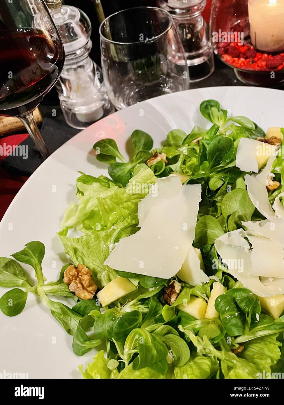 Gourmet-Salat mit italienischem Käse direkt am Restauranttisch mit einem Glas Rotwein Stockfoto