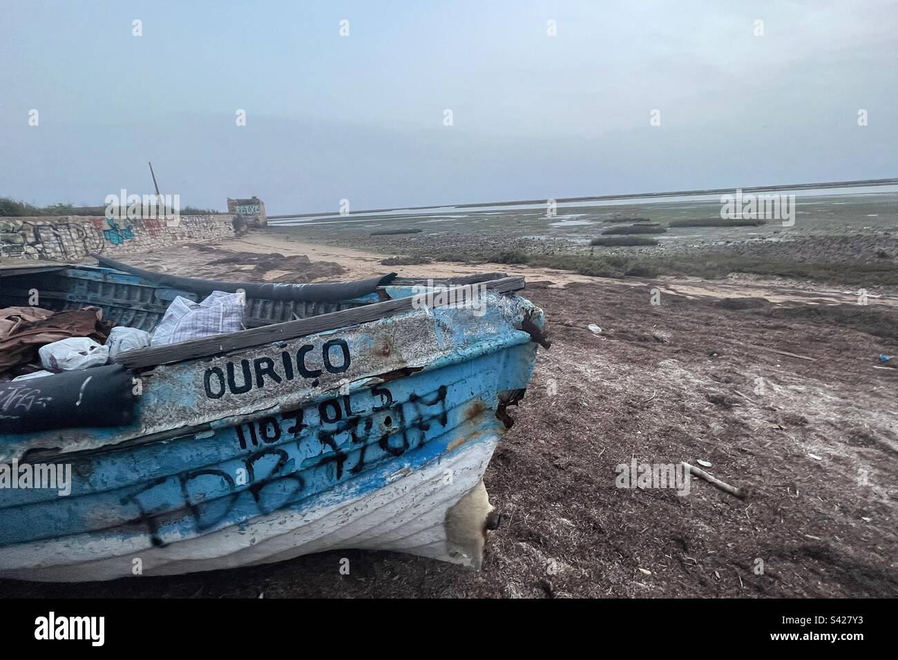 Stillgelegtes Fischerboot an der Küste von Faro in Portugal mit Graffiti auf Schlammflächen Stockfoto
