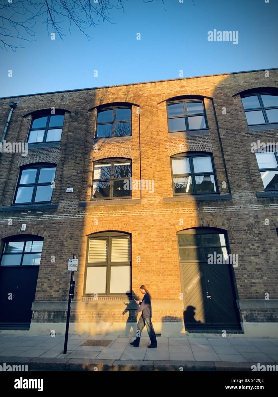 Ein Mädchen geht durch die Nachmittagssonne auf einem Industriegebäude in London Stockfoto