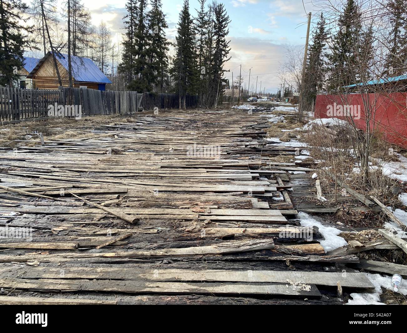 Eine Straße aus Holzplanken in einer Dorfstraße zwischen Häusern im Norden Russlands in Yakutia. Stockfoto