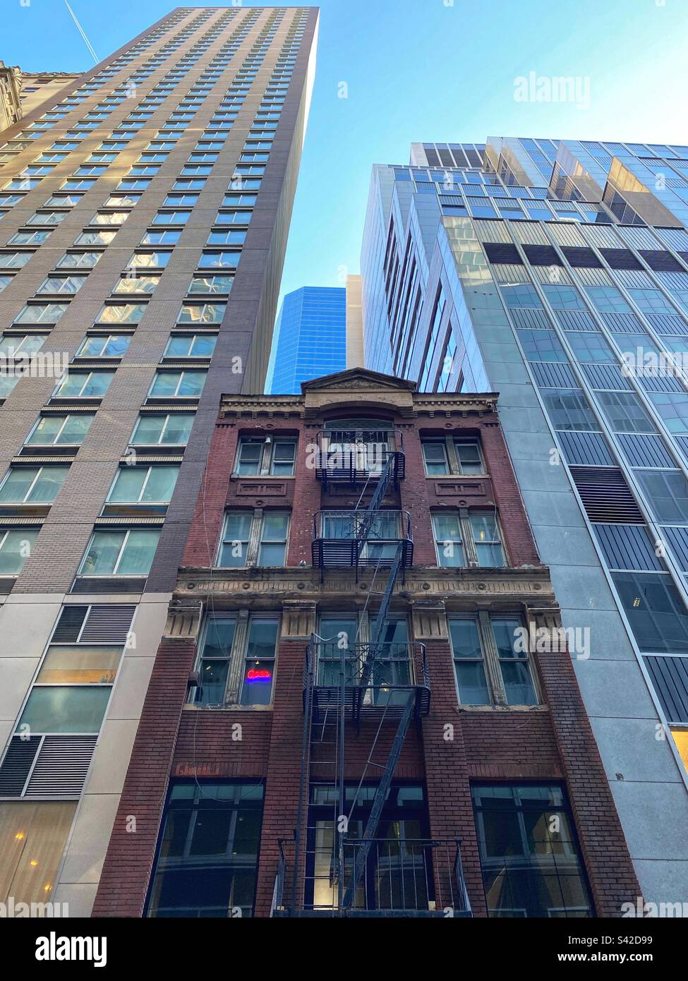 Ein altes Backsteingebäude mit einer Feuertreppe zwischen modernen Wolkenkratzern in Lower Manhattan Stockfoto