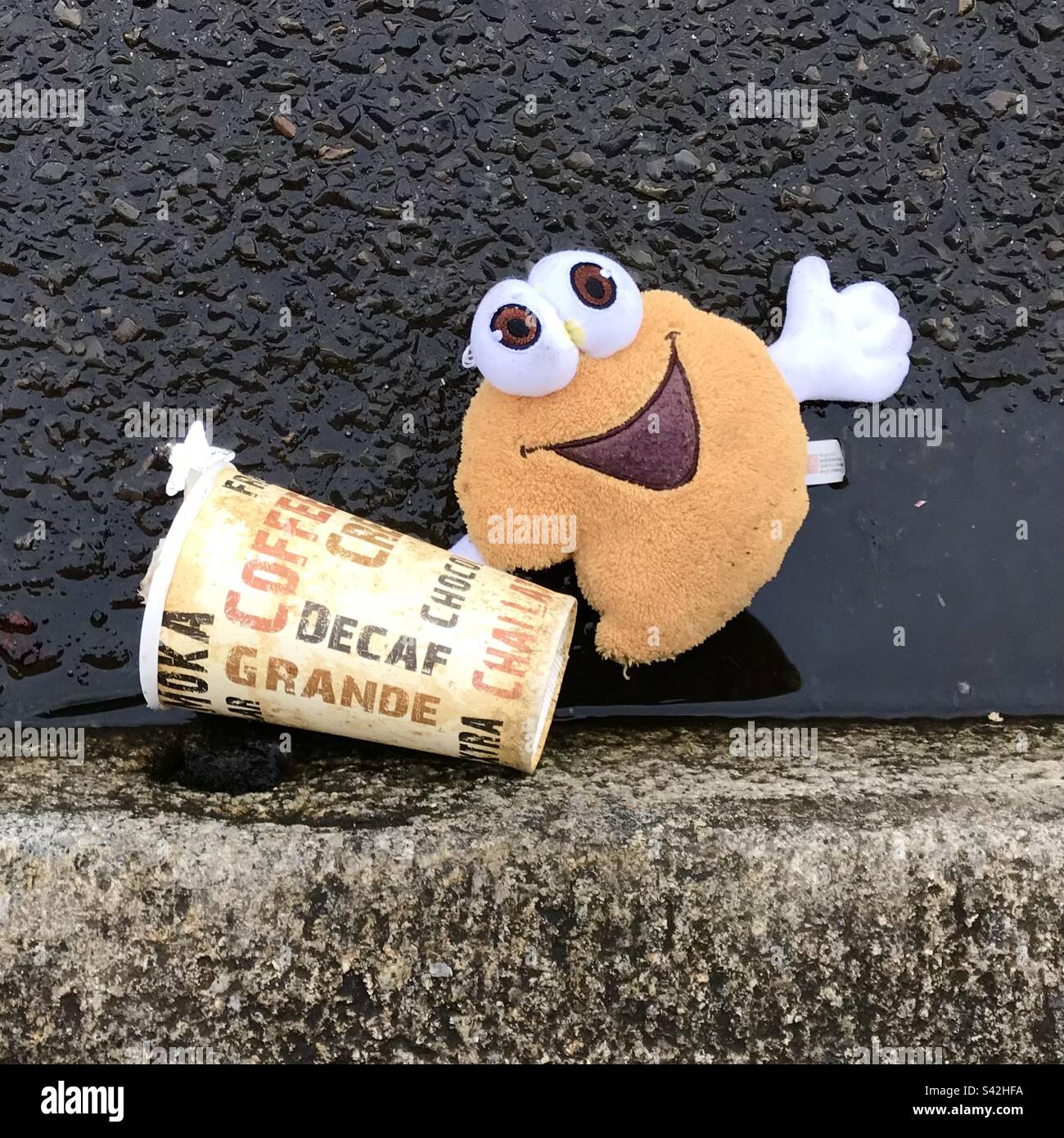 In der Gosse. Weggeworfene Kaffeetasse aus Papier und lächelnde Gesichts-Emoji Stockfoto