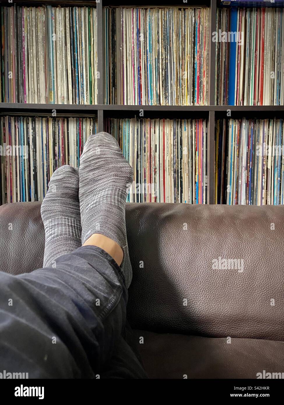 Eine große Schallplattensammlung Albumärmel auf Regalen Mann sitzt mit gekreuzten Beinen auf dem Ledersofa Stockfoto