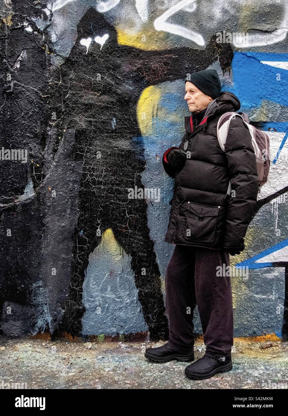 Er ist hinter dir! Warm gekleideter alter Mann an der Graffiti-Mauer in Mauerpark, Berlin Stockfoto