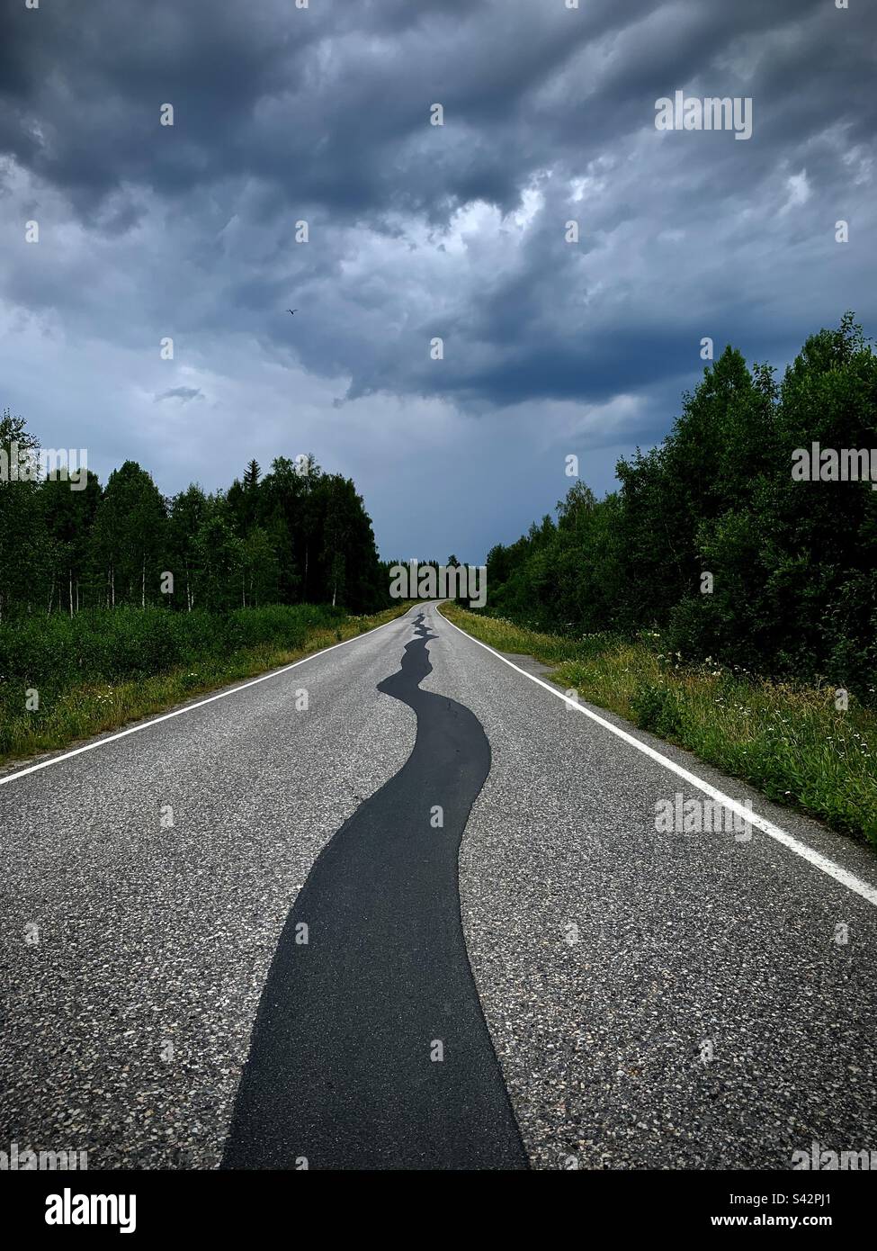 Eine dunkle, grüblerische Autobahn mit schwarzschlangenartigem Asphalt, der sich mitten auf der Straße in einen grüblerischen stürmischen Himmel im untergangsgeladenen Kajaani in Finnland schlängelt Stockfoto
