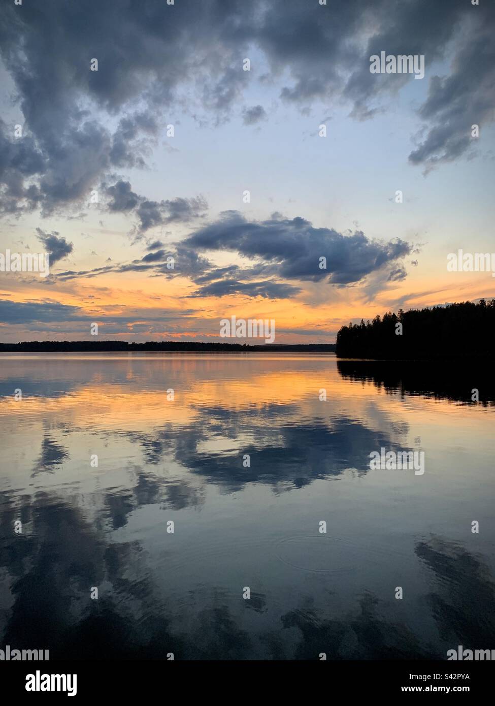 In der finnischen Kajaani-Region während eines arktischen Sommers reflektieren sich brodelnde dunkle Sturmwolken in einem großen See während der Mitternachtssonne Stockfoto