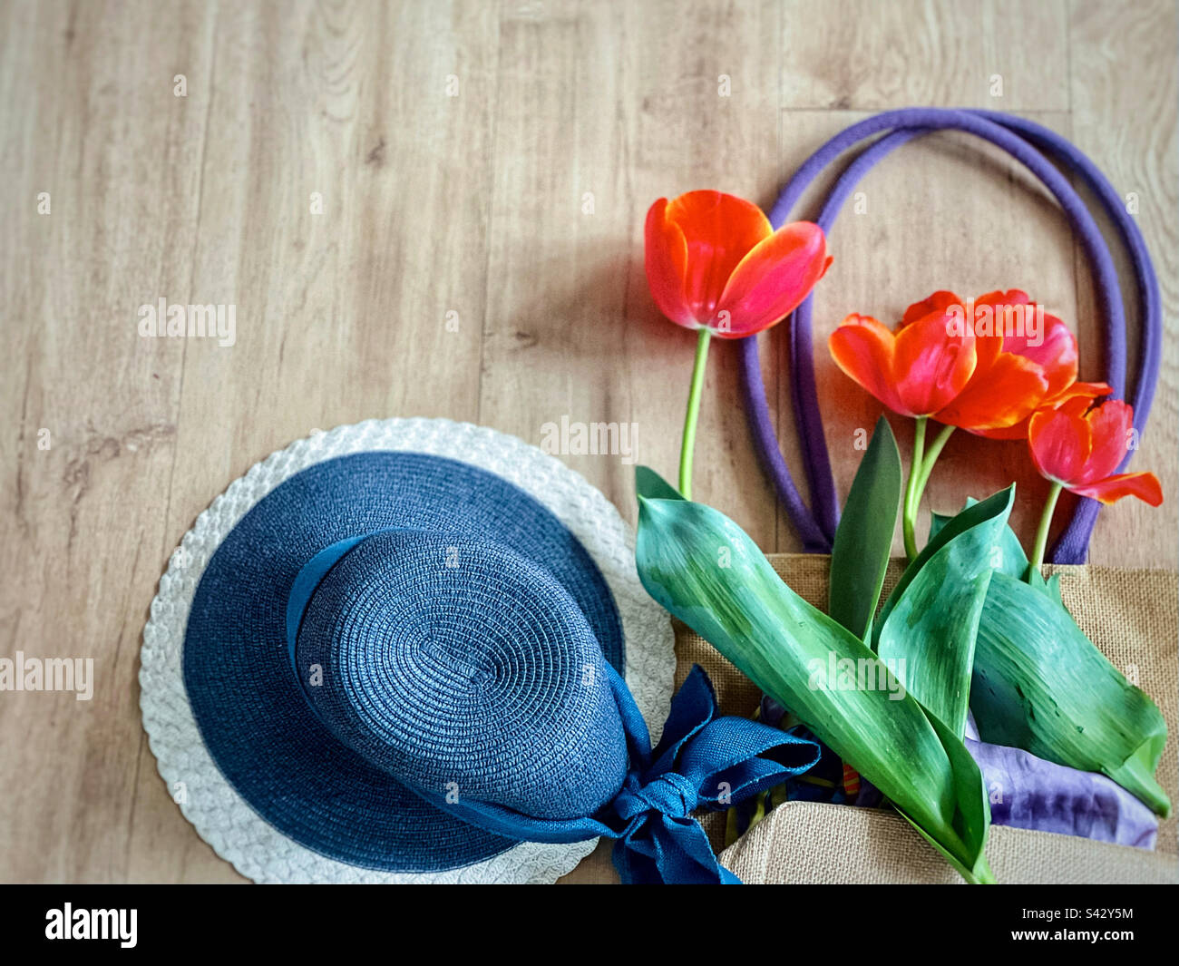Flache Lage mit orangefarbenen Tulpen auf einem Strohbeutel neben einem Strohhut. - Smartphone-aufgenommenes Stockfoto