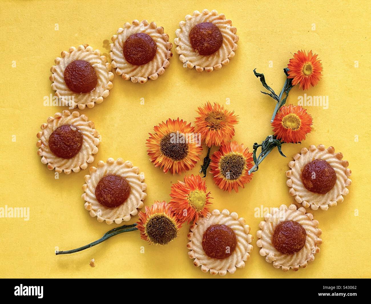 Flache Lage von Marmeladentörtchen und Strohblumen auf gelbem Hintergrund. Stockfoto