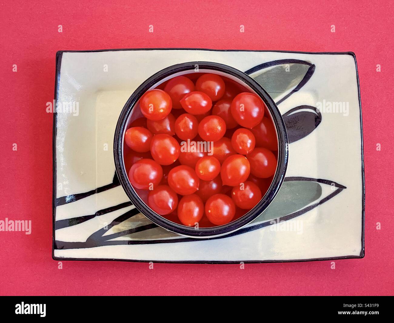 Direkt über dem Blick auf Kirschtomaten in der Schüssel auf dem Teller auf rotem Hintergrund. - Smartphone-aufgenommenes Stockfoto