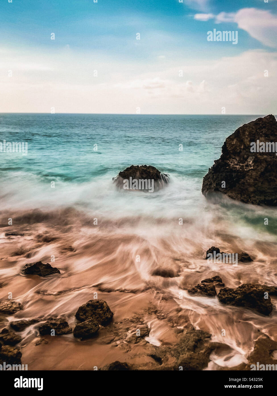 Wellen brechen auf den felsigen Strand gegen Meer, Himmel und Horizont in Bali, Indonesien. Stockfoto