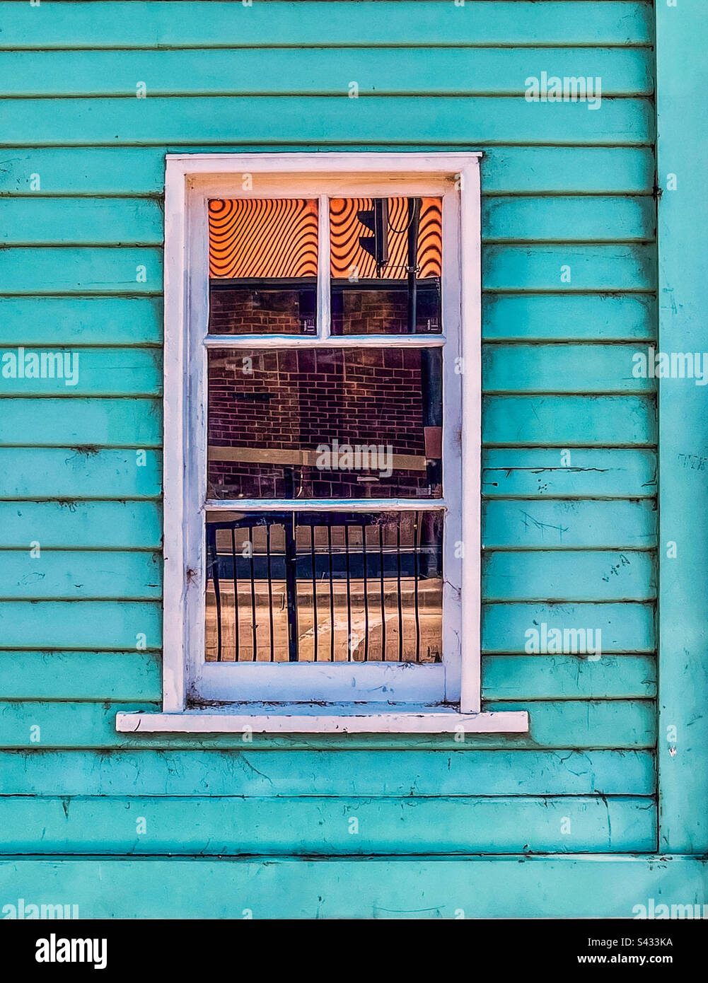 Nahaufnahme von Straßenreflexionen in einem einzigen, geschlossenen Fenster mit blauer Holzfassade. Stockfoto