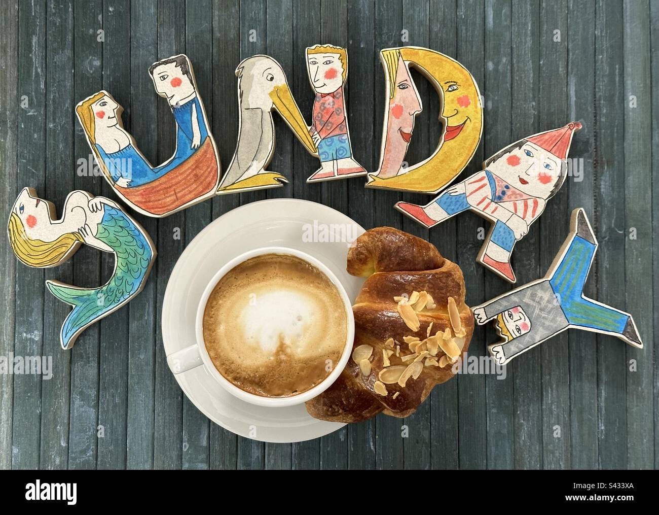Sonntags kreatives Frühstück mit handgemalten lustigen Holzbuchstaben, Cappuccino und Croissant an der Bar Stockfoto