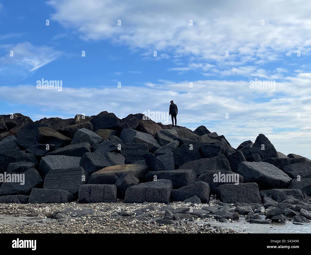 Ein Mann, der auf Felsen am Meer steht, vor einem blauen Himmel Stockfoto