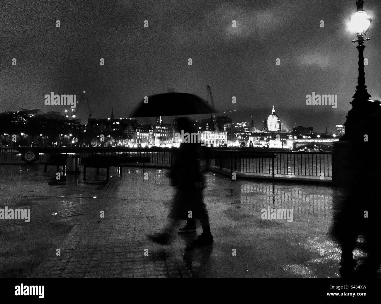Leute mit Sonnenschirmen, die in einer regnerischen Nacht am Südufer Londons vorbeilaufen Stockfoto
