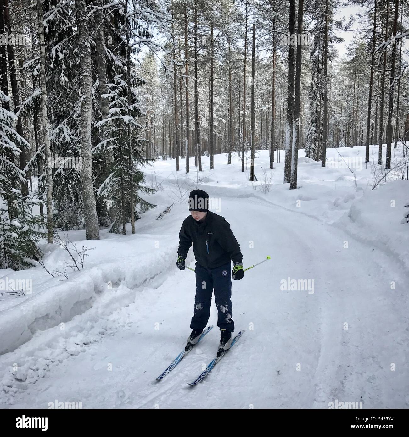 Ein kleiner Junge, der im tiefen Winter im subarktischen Kreis von Kajaani in Finnland auf einer abgelegenen Landstraße bergab fährt Stockfoto