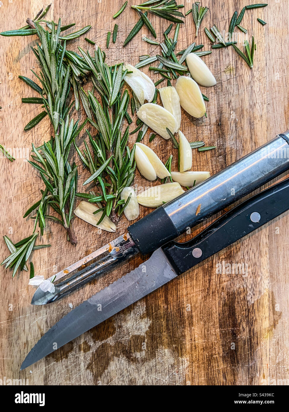 Schneidebrett mit Knoblauch und Rosmarin mit Messer und Gemüseschäler - Smartphone-aufgenommenes Stockfoto