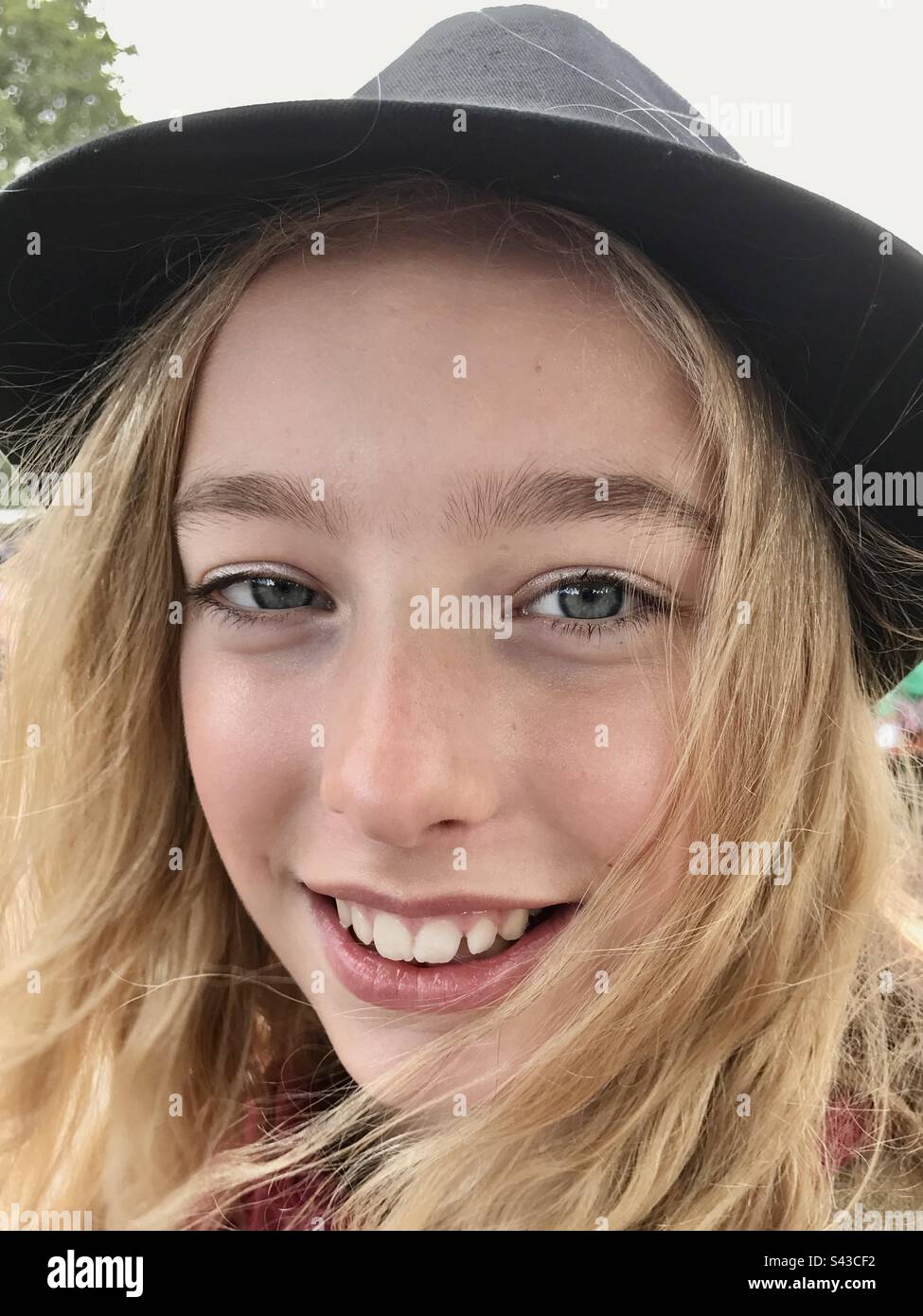 Ein Mädchen im Teenageralter, das vor Freude lächelt, in einem Fedora-Hut auf einem Musikfestival Stockfoto