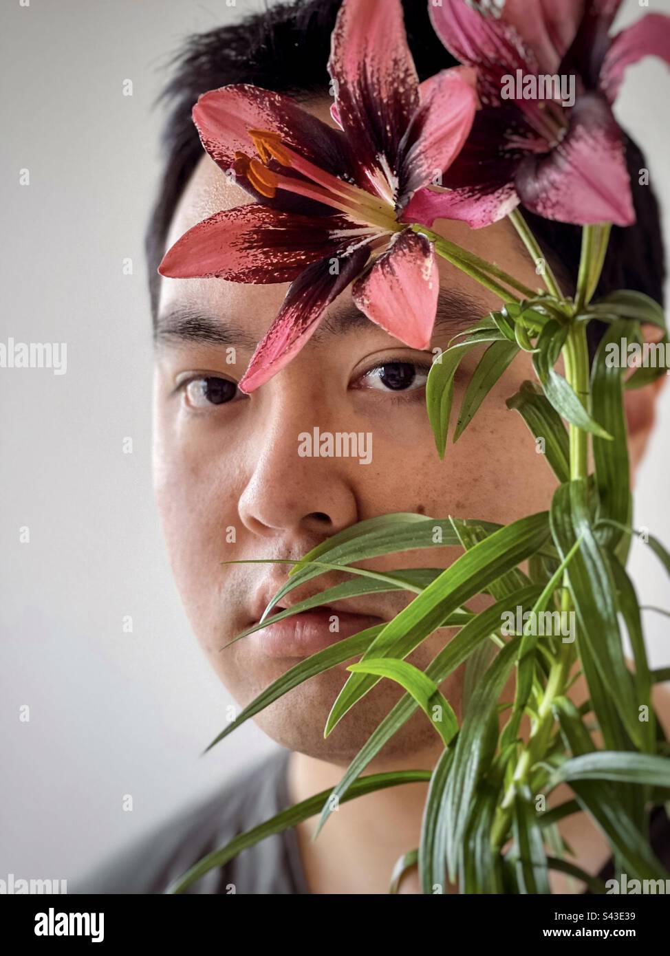 Nahaufnahme eines jungen Asiaten mit roten Lilien auf weißem Hintergrund. Stockfoto