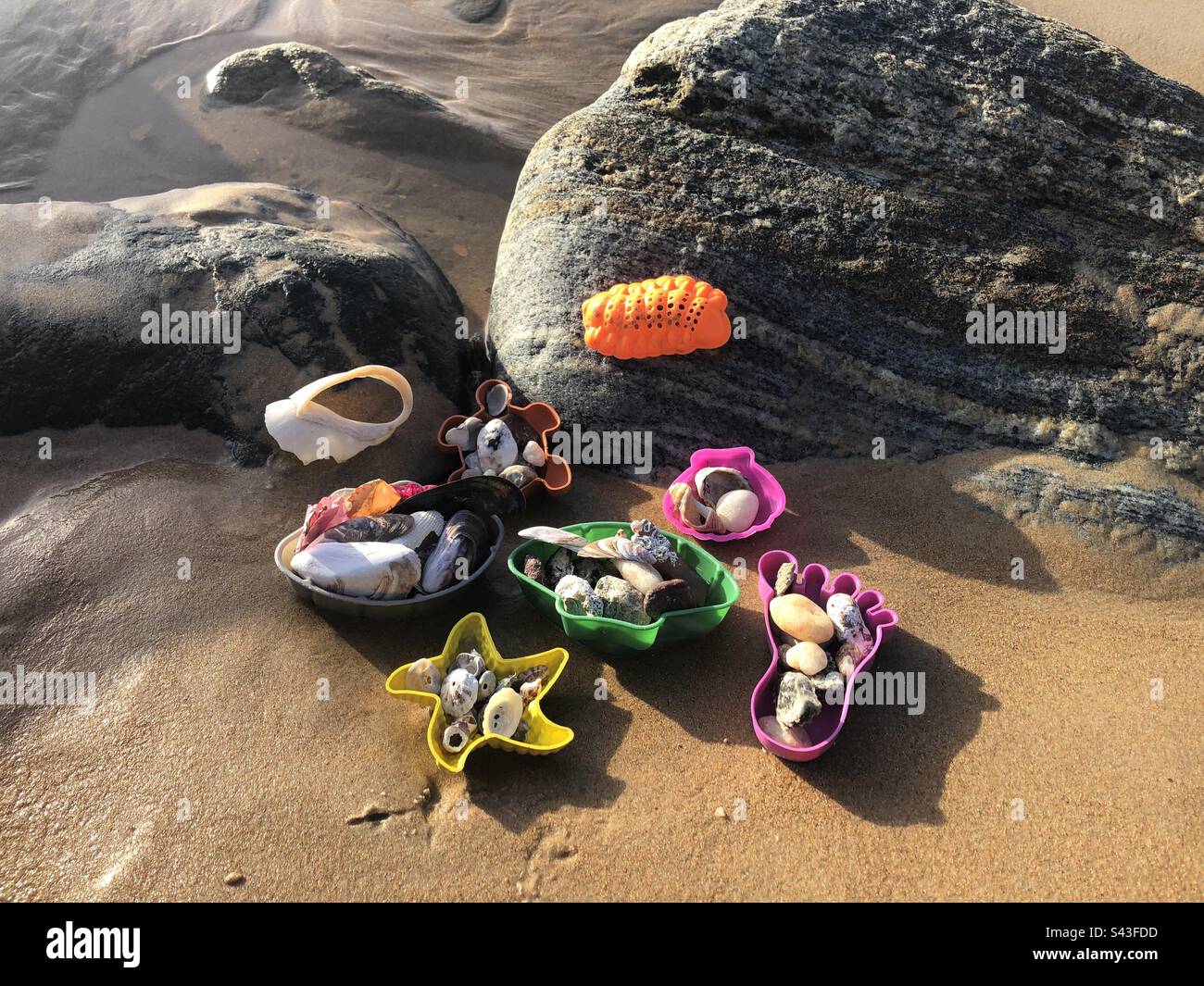 Strandspielzeug gefüllt mit Muscheln und Steinen im Sand. Stockfoto