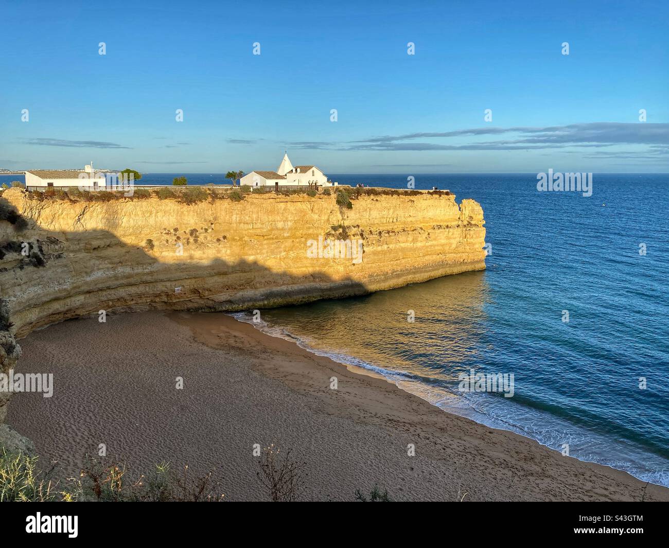 Blick auf den Sonnenuntergang an der weißen Kirche auf den Sandsteinklippen Senhora da Rocha und Praia Nova Beach in der Algarve, Portugal. Stockfoto