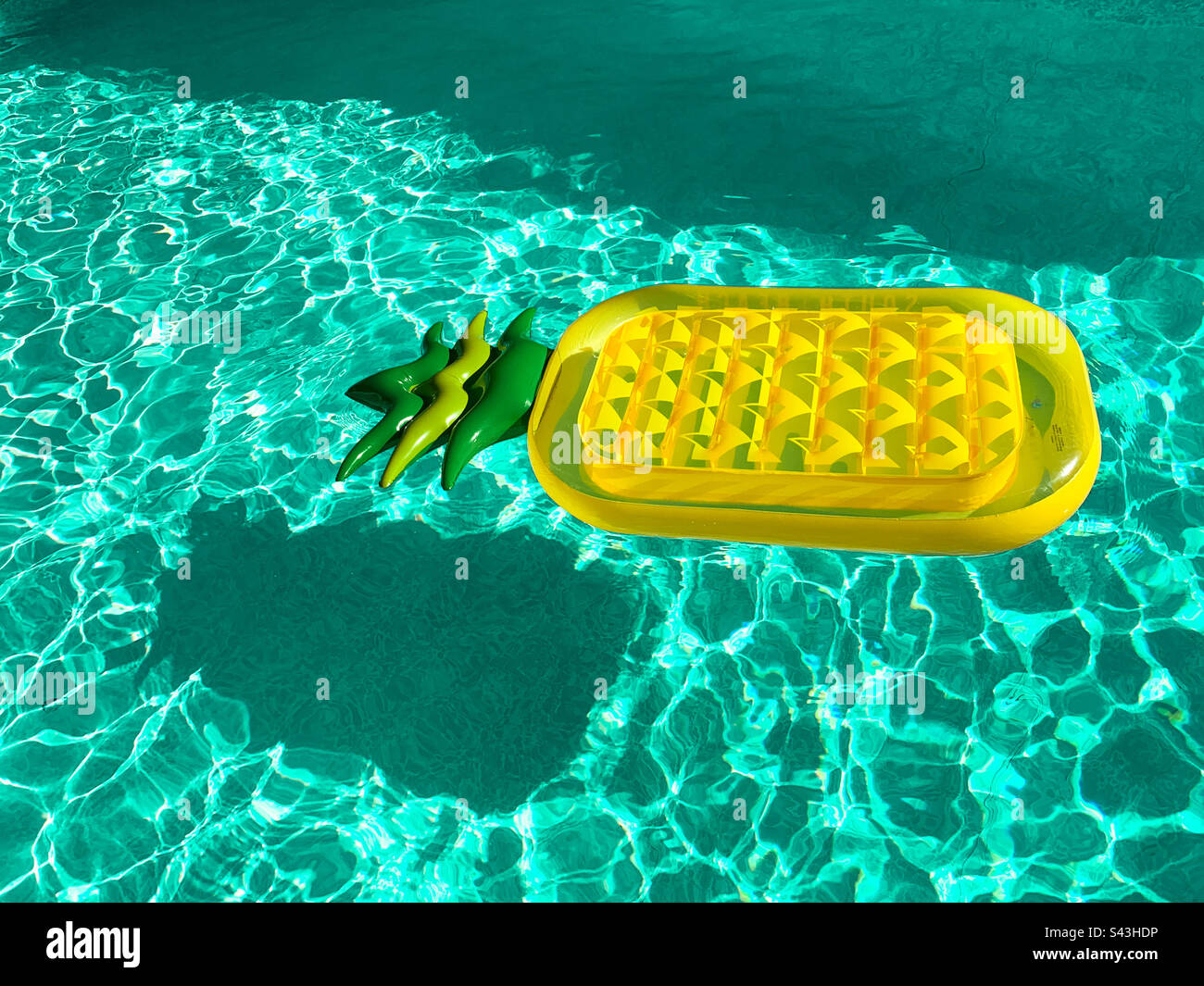 Blick aus einem hohen Winkel auf eine aufblasbare anananasförmige Matratze, die an einem sonnigen Tag im Swimmingpool schwimmt Stockfoto