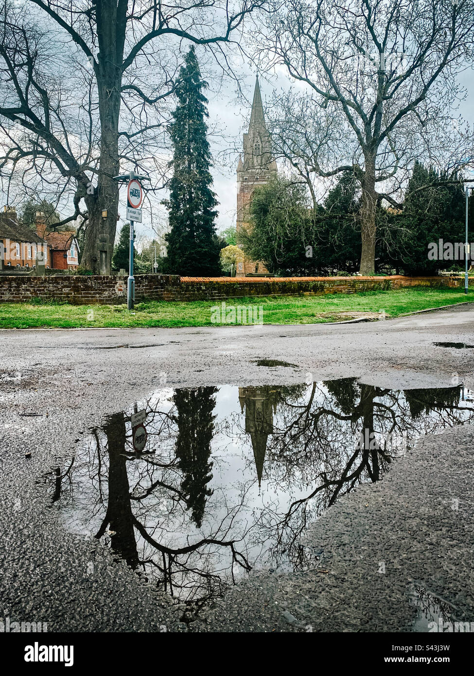 Eine Pfütze auf der Straße als Ergebnis der April-Schauer vor der St. Michael's Church in Tilehurst, Reading, Großbritannien Stockfoto