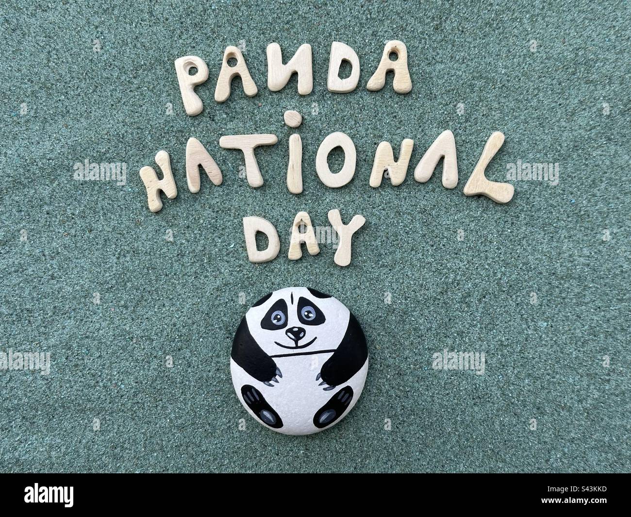 Der Panda-Nationalfeiertag wird mit handbemalten Panda auf einem Stein, handgefertigten Holzbriefen auf grünem Sand gefeiert Stockfoto