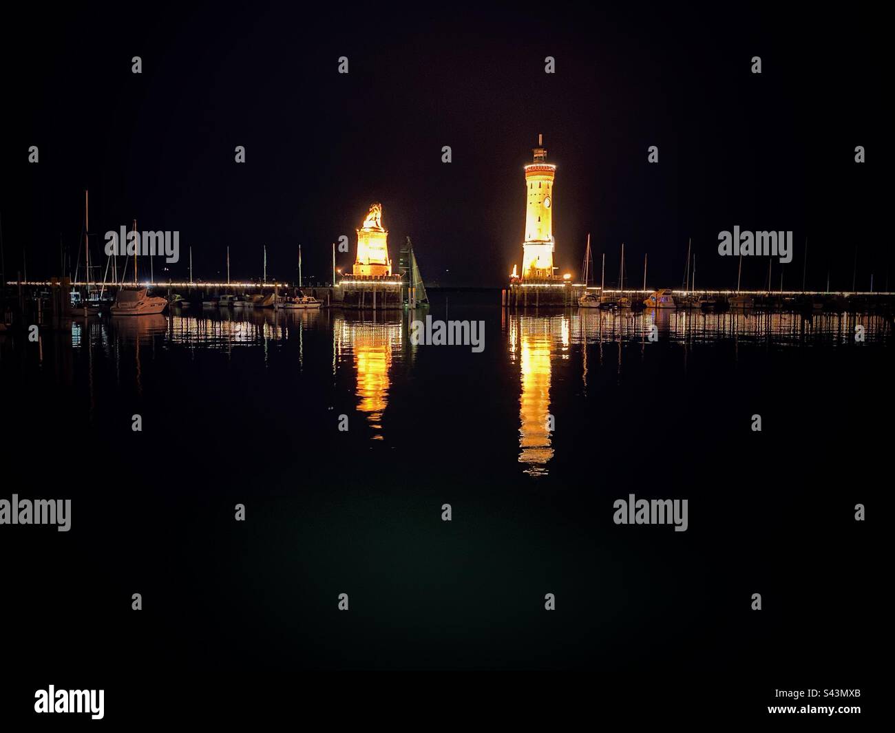 Nachtansicht auf die beleuchtete Löwenstatue und den Leuchtturm im Hafen von Lindau am Bodensee, Deutschland. - Smartphone-aufgenommenes Stockfoto