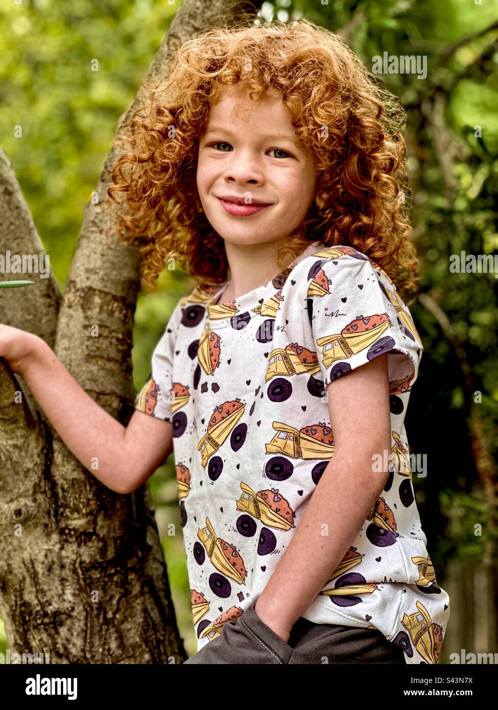 Kind mit roten Locken, das in einen Olivenbaum klettert Stockfoto