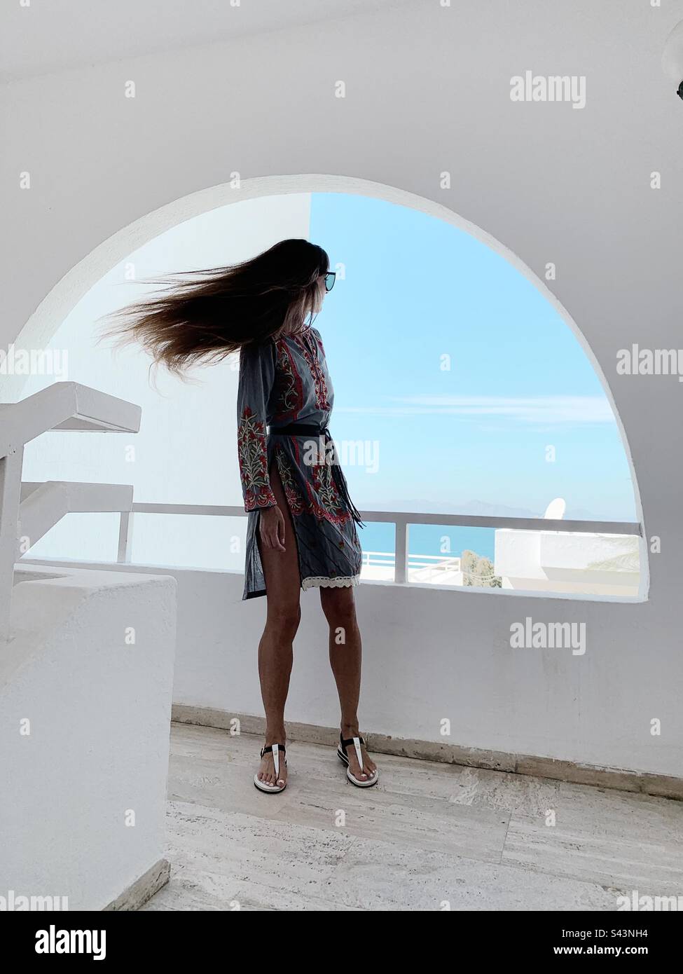 Wind im langen Haar einer jungen Frau, die am Fenster steht Stockfoto