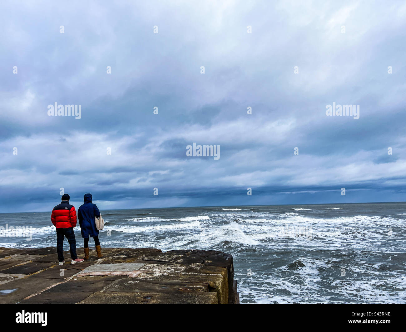 Ein Paar, das auf dem Whitby Pier in die Nordsee schaut Stockfoto