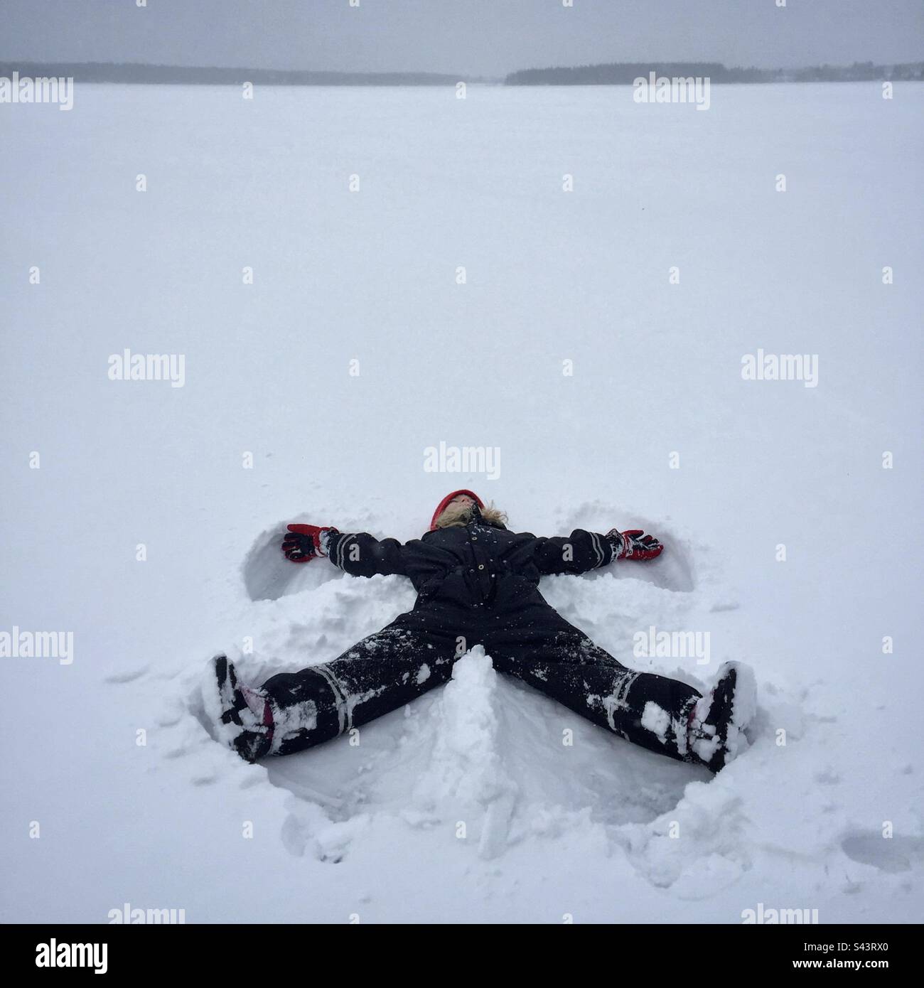 Ein 7-jähriges junges Mädchen, das im tiefen Winter einen Schneeengel auf einem riesigen gefrorenen See im subarktischen Kreis von Kajaani in Finnland macht Stockfoto