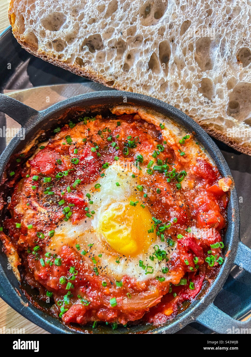 Backei-Shakshuka mit gebackenem Sauerteigbrot, serviert in Eisenpfanne Stockfoto