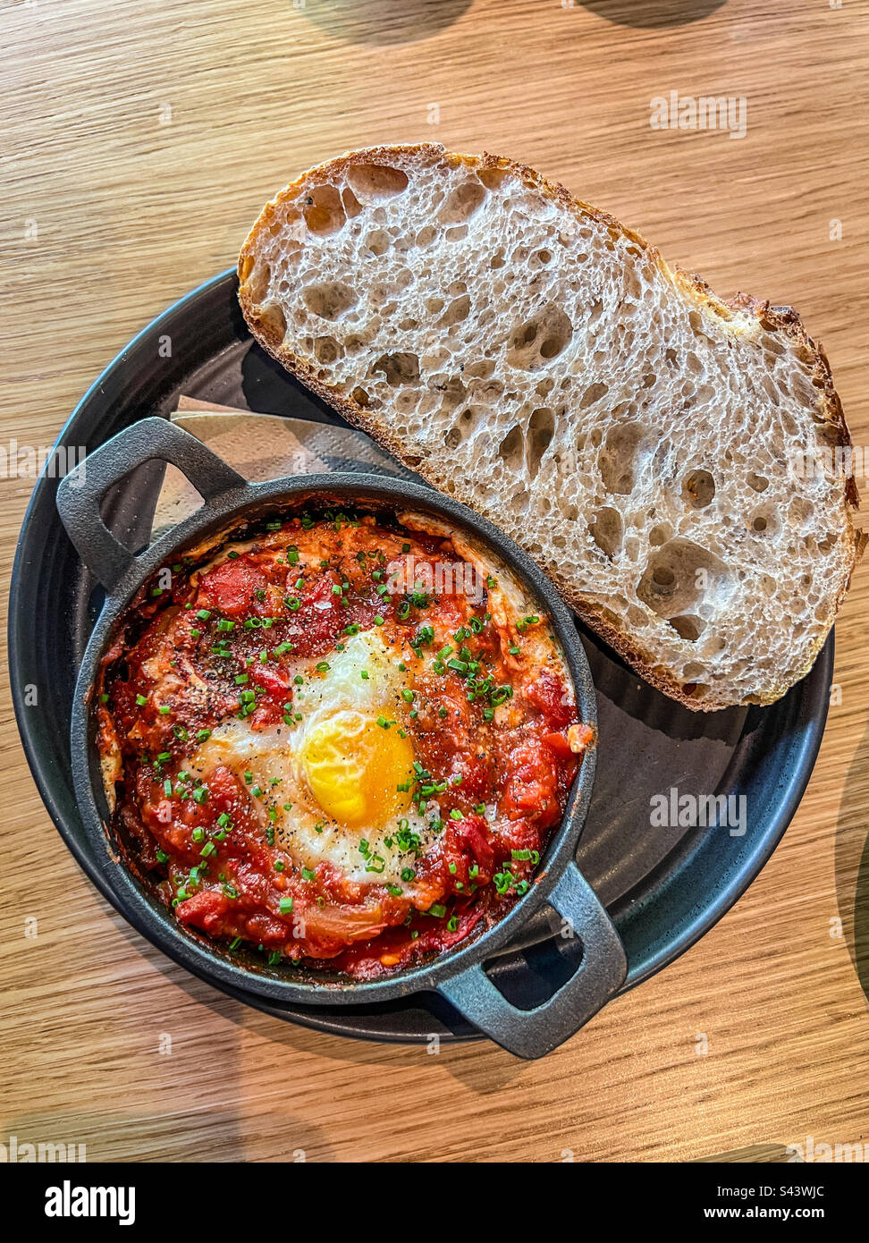 Backei-Shakshuka mit gebackenem Sauerteigbrot, serviert in Eisenpfanne Stockfoto
