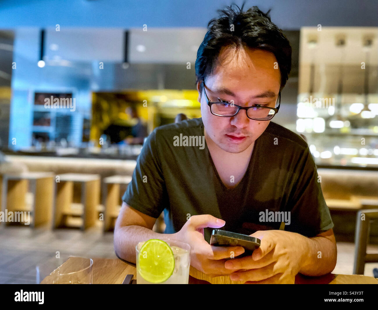 Ein junger asiatischer Mann mit Brille, der im Restaurant ein Smartphone am Tisch benutzt. Wireless-Technologie. Kommunikation. - Smartphone-aufgenommenes Stockfoto