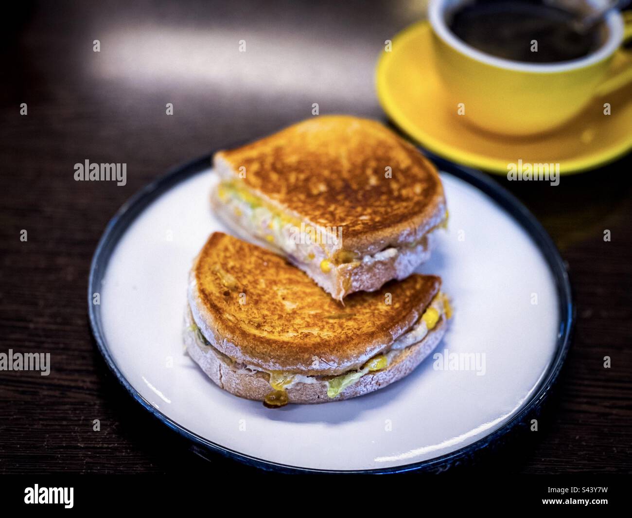 Blick aus einem hohen Winkel auf Thunfischkäse-Toasties auf dem Teller mit einer Tasse schwarzem Kaffee, selektiver Fokus. Komfortables Frühstück. Stockfoto