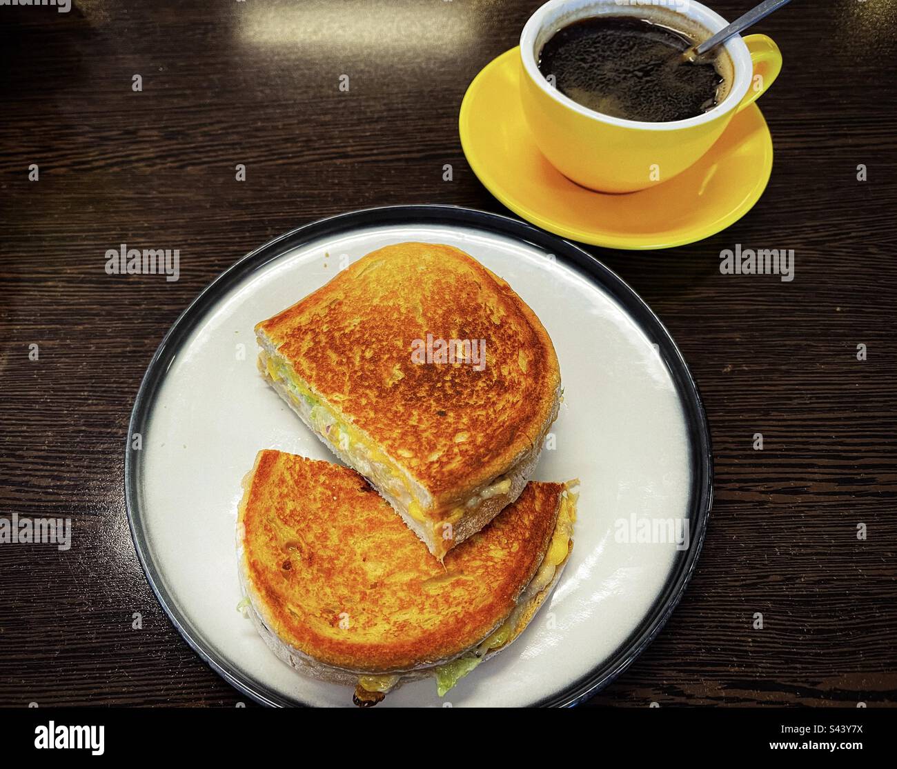 Blick aus einem hohen Winkel auf Thunfischkäse-Toasties auf dem Teller mit einer hellgelben Tasse langen schwarzen Kaffees auf dem Tisch. Komfortables Frühstück. Stockfoto