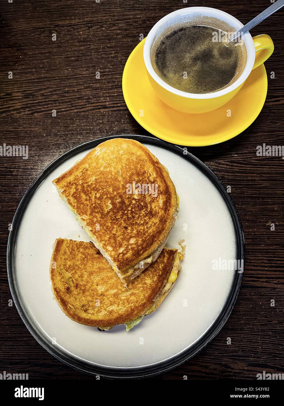 Blick aus dem hohen Winkel auf Thunfischkäse-Toasties auf dem Teller mit einer hellgelben Tasse heißem Kaffee auf dem Tisch. Komfortables Frühstück. Stockfoto