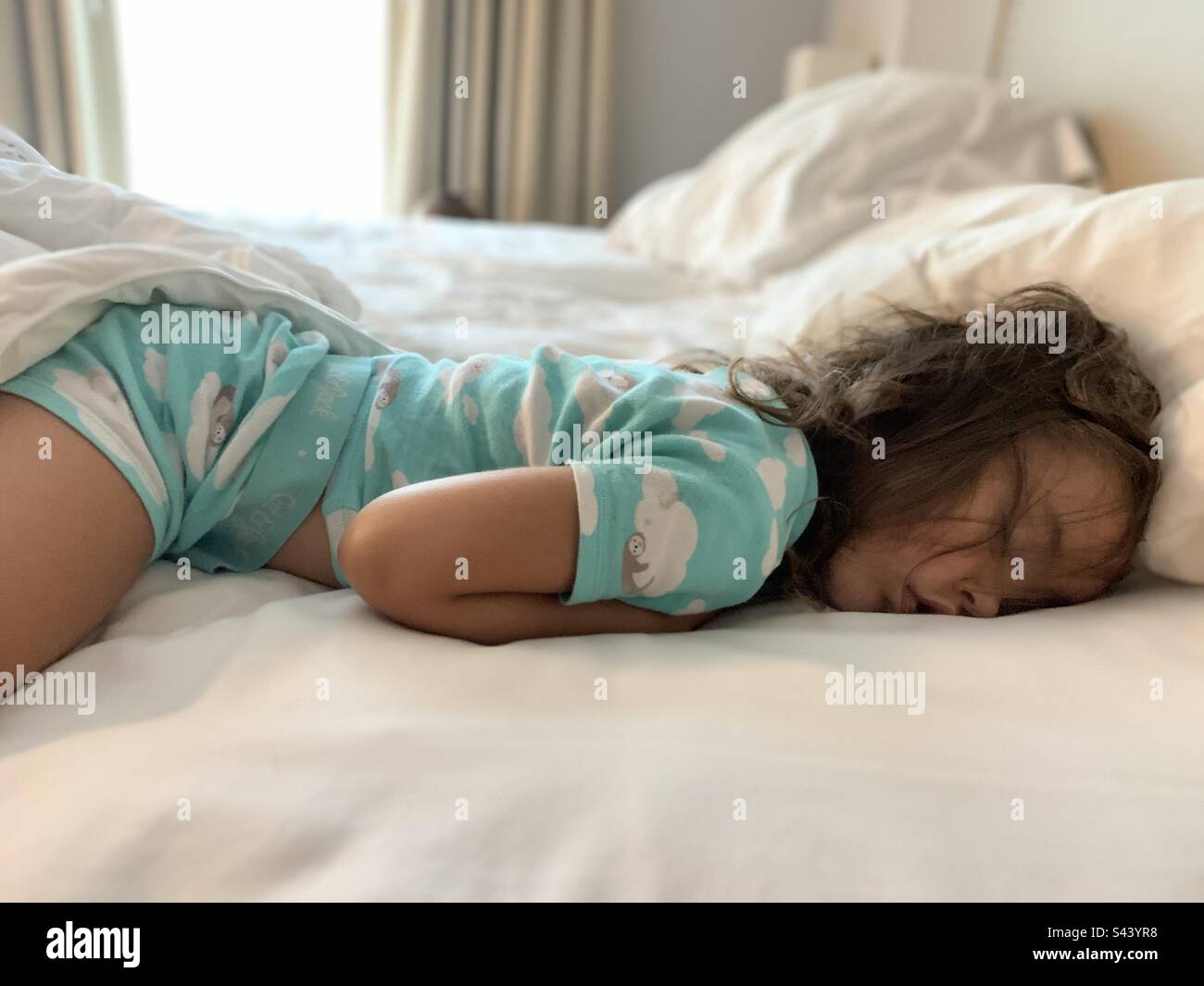 Ein kleines Mädchen schläft in weißen Laken mit schmutzigen Haaren. Stockfoto