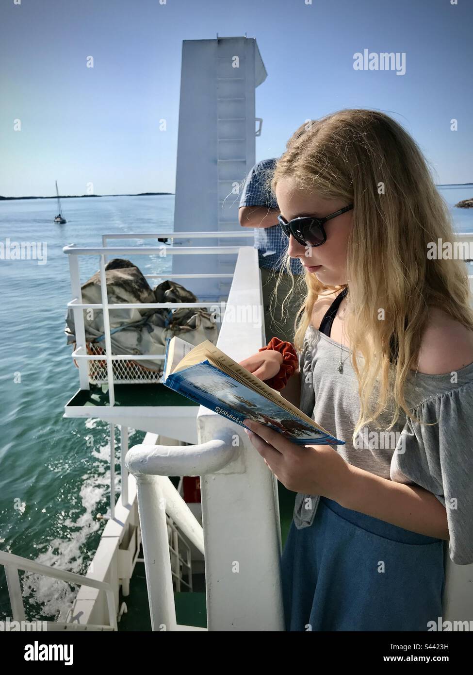 Bücherwurm eines jungen 10-jährigen Mädchens, das im Sommer auf einem öffentlichen Kreuzfahrtschiff auf den Åland-Inseln an der Ostsee ein Buch liest Stockfoto