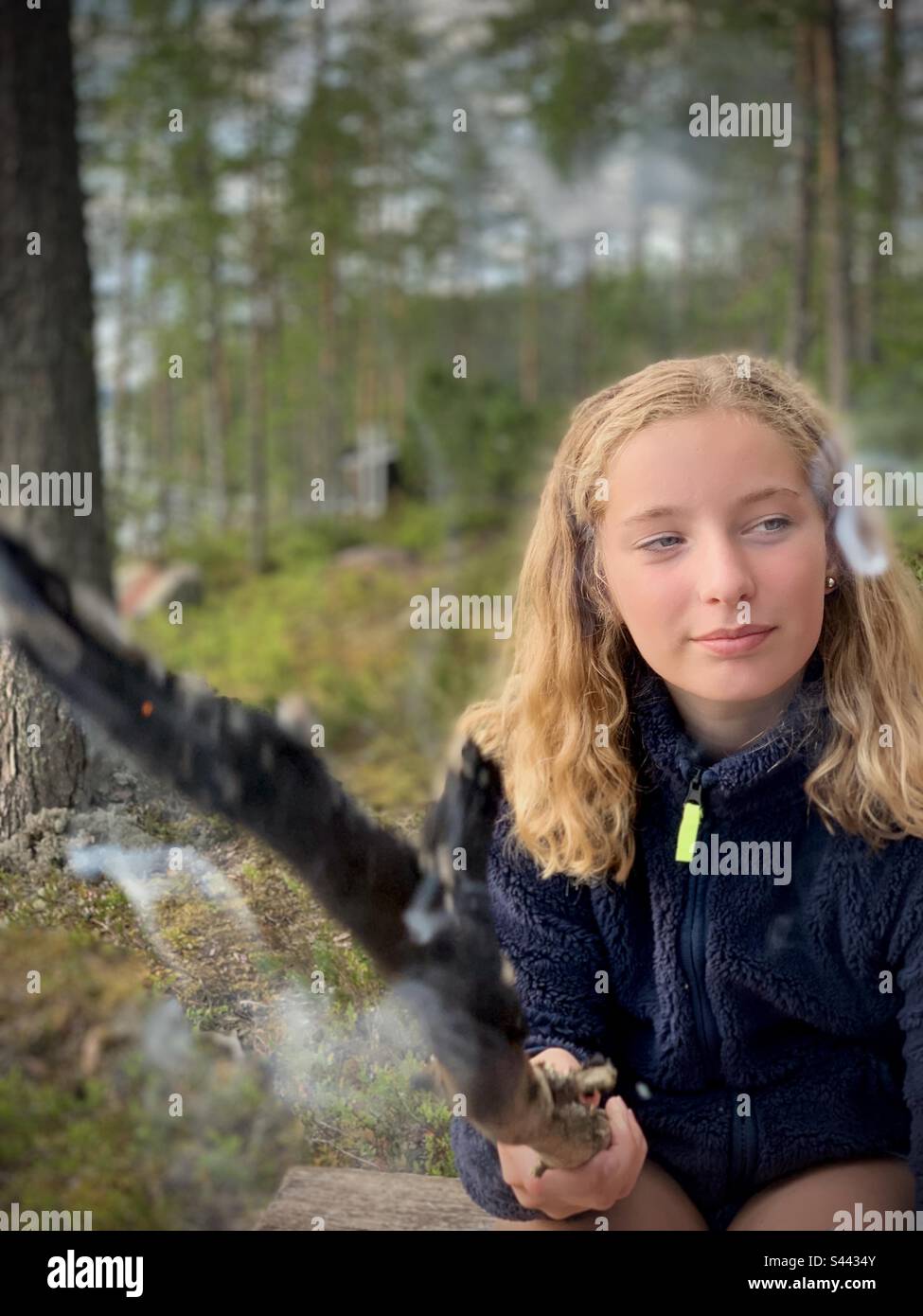Porträt einer 11-jährigen Teenagerin an einem Lagerfeuer in der Natur, die während eines arktischen Sommers mit einem brennenden Stock im Sommerhaus in der finnischen Kajaani-Region zeltet Stockfoto