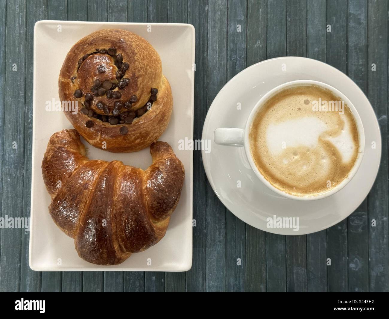 Üppiges italienisches Frühstück mit einem heißen Cappuccino, einem Croissant und einem Schokoladenwirbel an der Bar Stockfoto