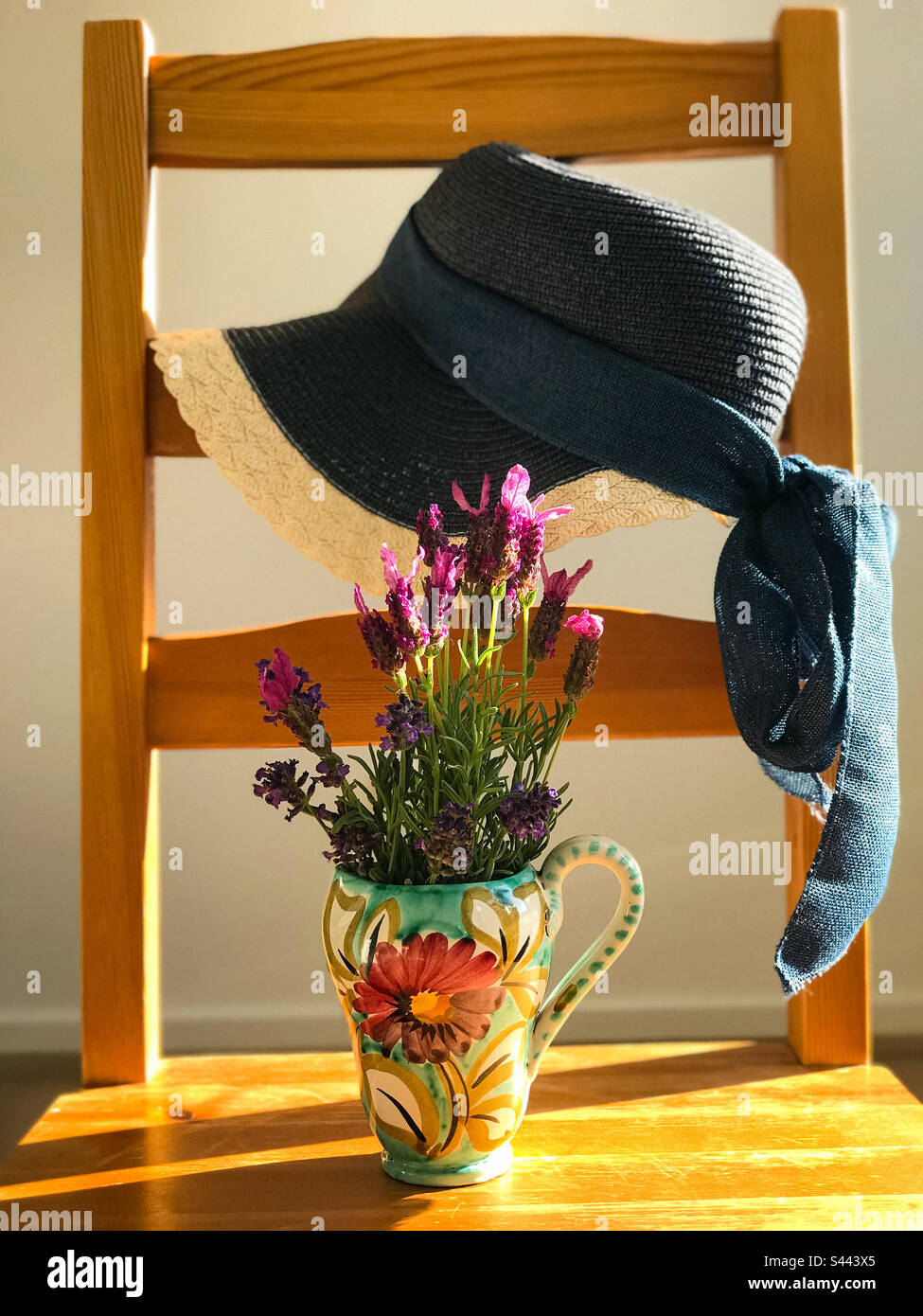 Blauer Strohhut und frische Lavendelblumen in Vintage-Vase auf Holzstuhl. Sommerthema. Art. Nahaufnahme. - Smartphone-aufgenommenes Stockfoto