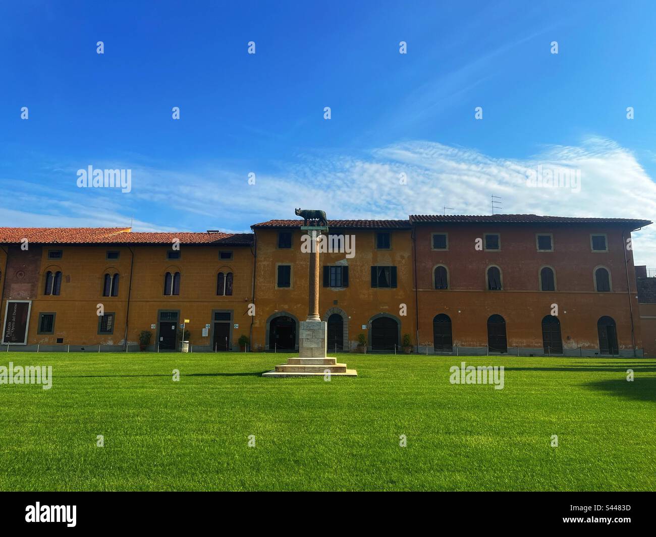 Romulus und Remus mit Wolfsstatue auf einer Säule in Pisa, Italien, Gebäuden im Hintergrund Piazza dei Miracoli und einem makellosen Rasen. Stockfoto