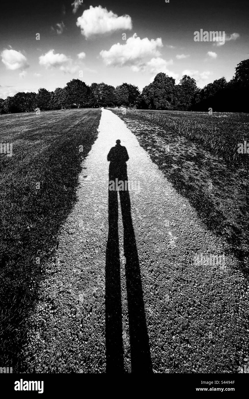 Eine Figur, die lange Schatten auf einem Schotterweg wirft Stockfoto