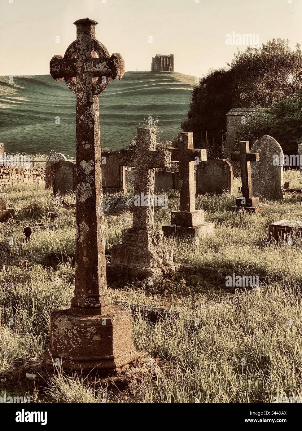 Stimmungsvoller Friedhof bei Sonnenuntergang mit überwuchertem Gras und Katharinenkapelle auf dem Hügel. Grabsteine der Nikolaikirche, Abbotsbury Dorset England Stockfoto