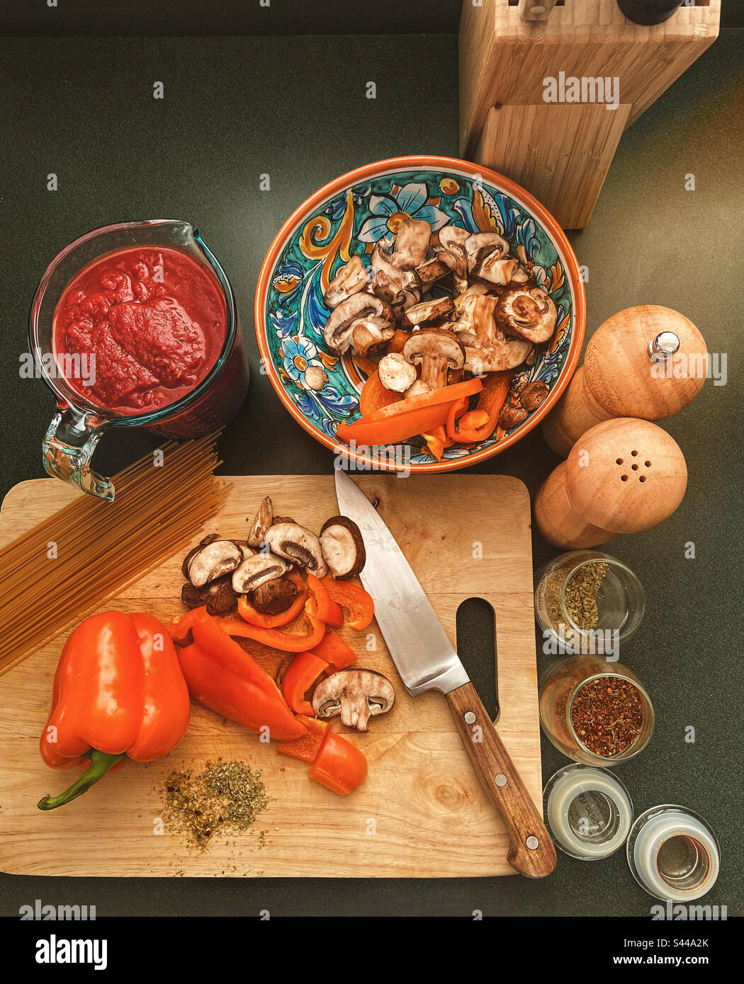 Italienische Speisen Zubereiten Sie pürierte Tomaten in einem Messbecher, geschnittene Pilze und Paprika auf einem Holzschneidebrett mit Messer, Salzstreuer, Pfeffermühle, Gewürze, Pasta auf der Küchentheke, von oben gesehen. - Smartphone-aufgenommenes Stockfoto