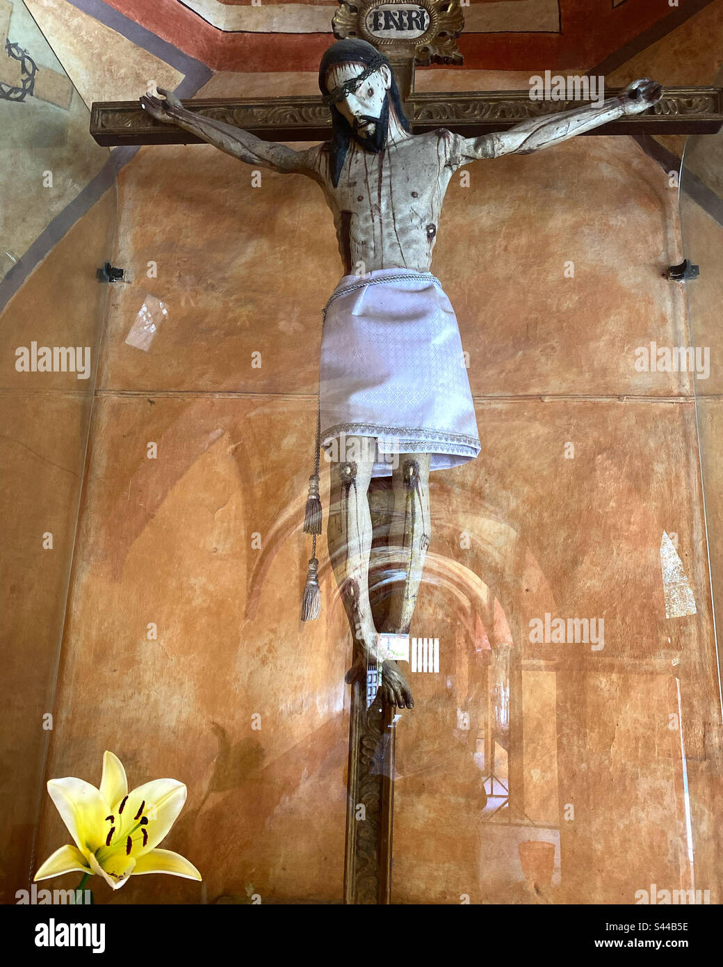 Eine gelbe Lilie oder lirio-Blume schmückt einen Altar mit einer Skulptur von Jesus Christus, gekreuzigt in San Miguel Toliman, Queretaro, Mexiko Stockfoto